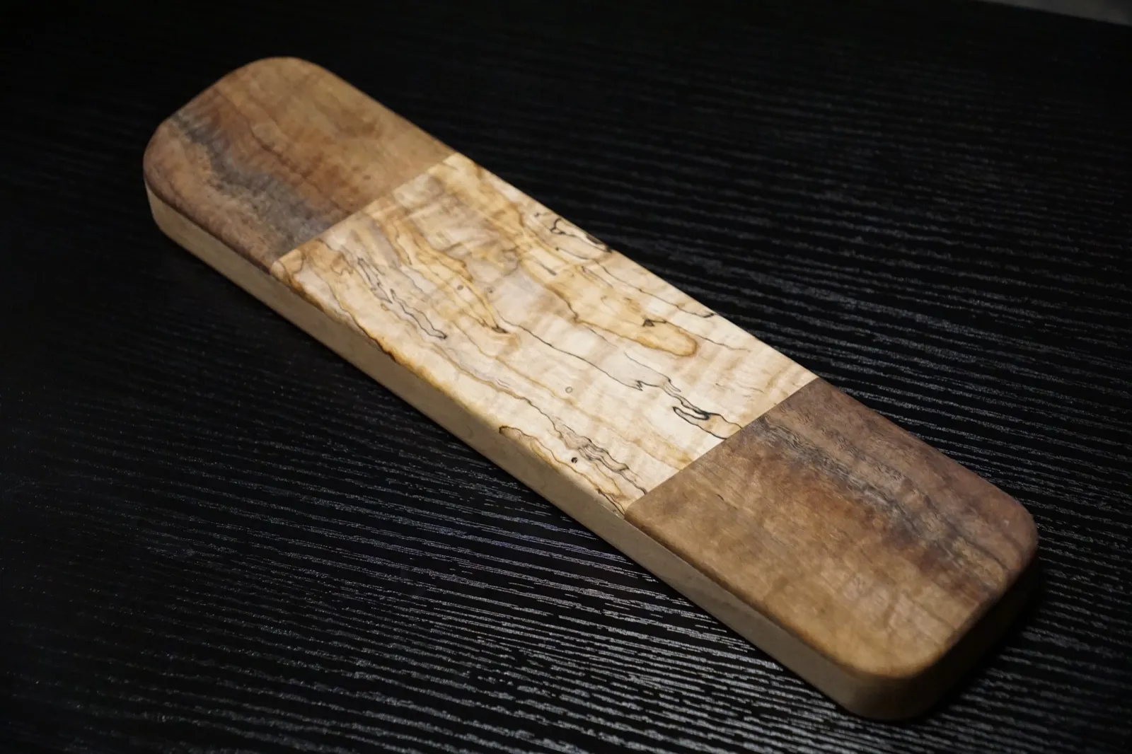 Rectangular clapper with curly walnut ends and a spalted maple center, on a black bench