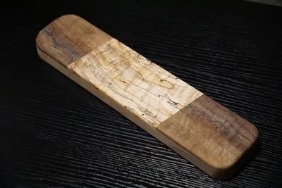 Rectangular clapper with curly walnut ends and a spalted maple center, on a black bench
