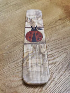 Long spalted maple clapper with an inlaid ladybug of red and dark wood between two walnut bands